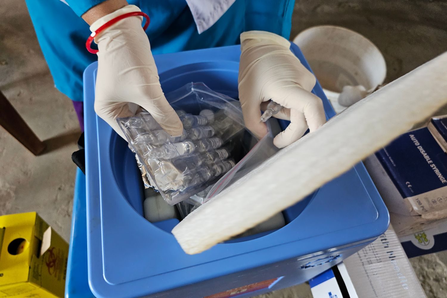 Profesional de salud con guantes retirando dosis de un refrigerador de vacunas en un centro de salud
