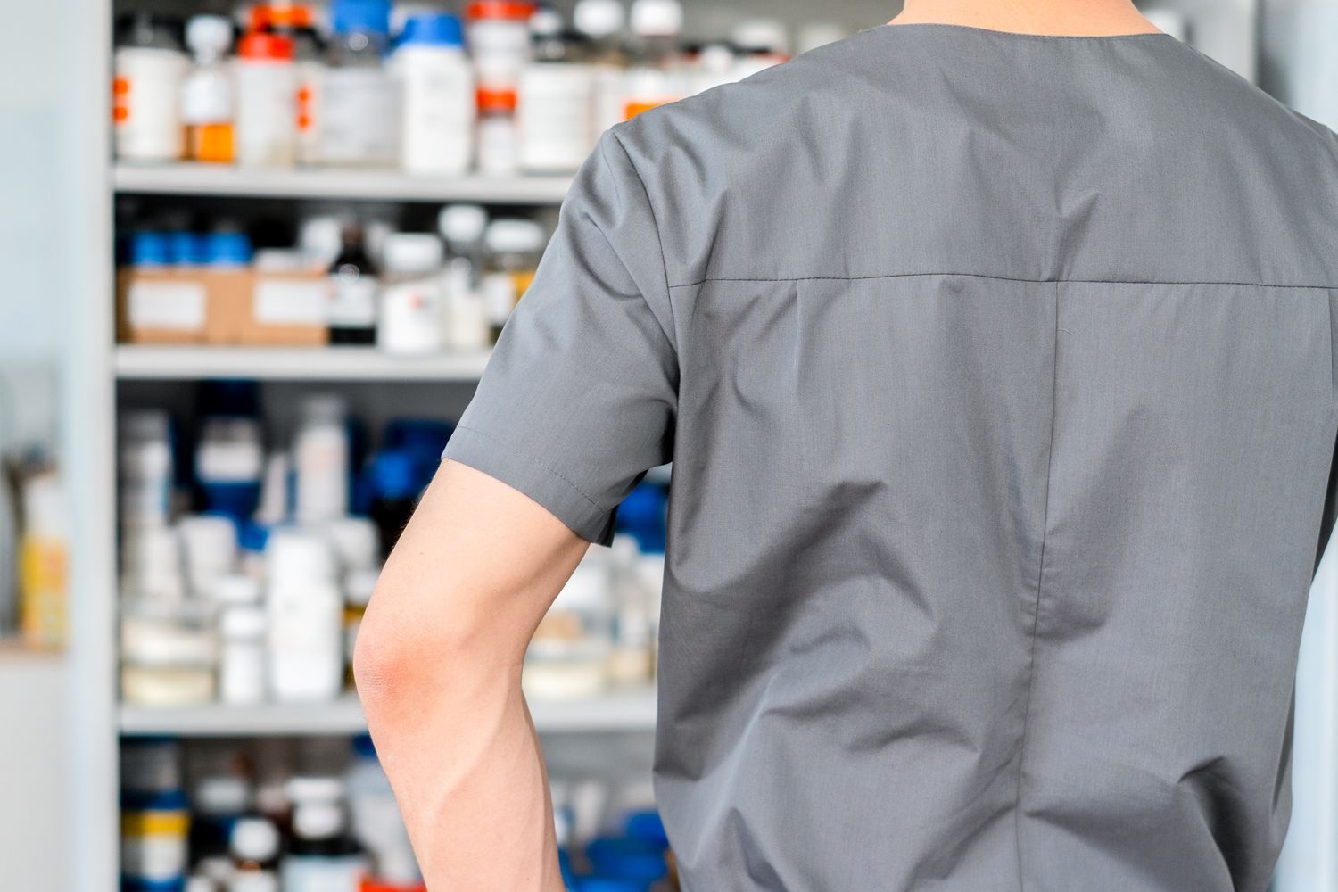 Trabajador de farmacia de espaldas frente a un mueble con frascos y cajas de medicamentos almacenados
