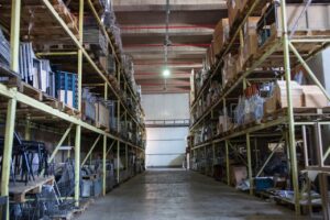 Pasillo central de una bodega de almacenamiento con estanterías metálicas altas y pallets de cajas de cartón envueltos en film