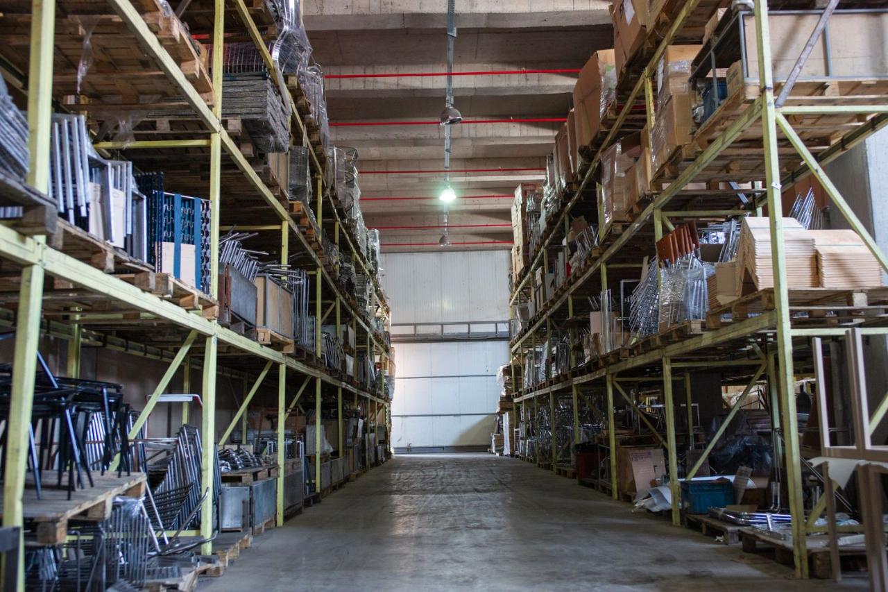 Pasillo central de una bodega de almacenamiento con estanterías metálicas altas y pallets de cajas de cartón envueltos en film